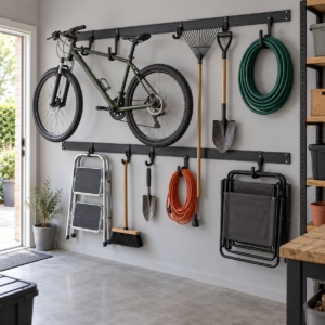 Two black steel wall rails with hooks holding a bicycle, ladder, rake, spade and hoses in a garage